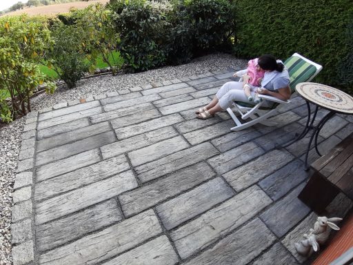 Eine Person sitzt in einem Liegestuhl auf einer gepflasterten Terrasse.