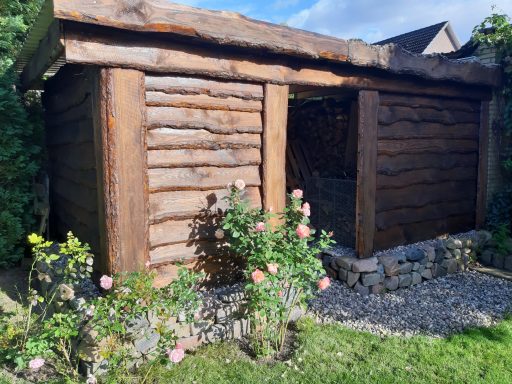 Holzhütte mit natuurligen Wänden, umgeben von Rosen und Kiesboden.